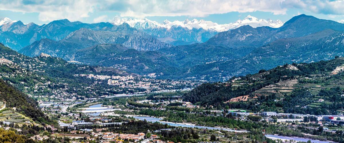 A mountainous landscape with a river winding through a valley, surrounded by snow-capped peaks and dense forests.