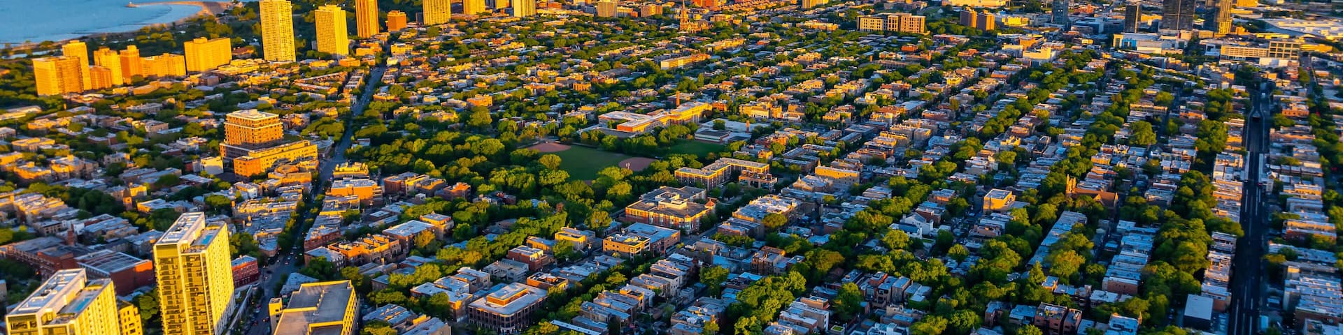 Green uptown and high-rise downtown of Chicago, Illinois in the rays of setting sun. Amazing blue waterscape of Lake Michigan at backdrop.