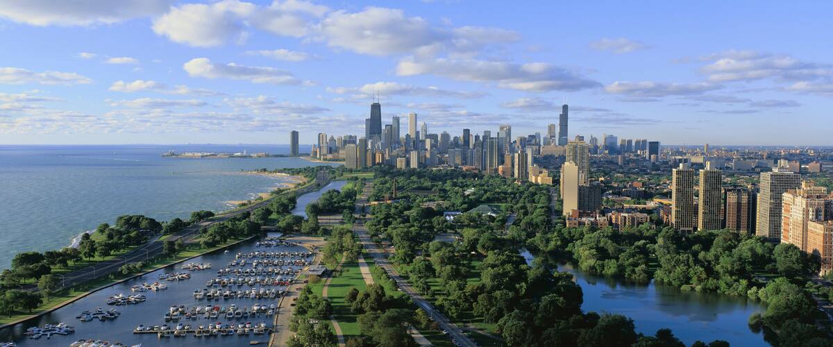 This shows Lincoln Park, Diversey Harbor with its moored boats, Lake Michigan to the left and the skyline in summer. There is morning light on the city.