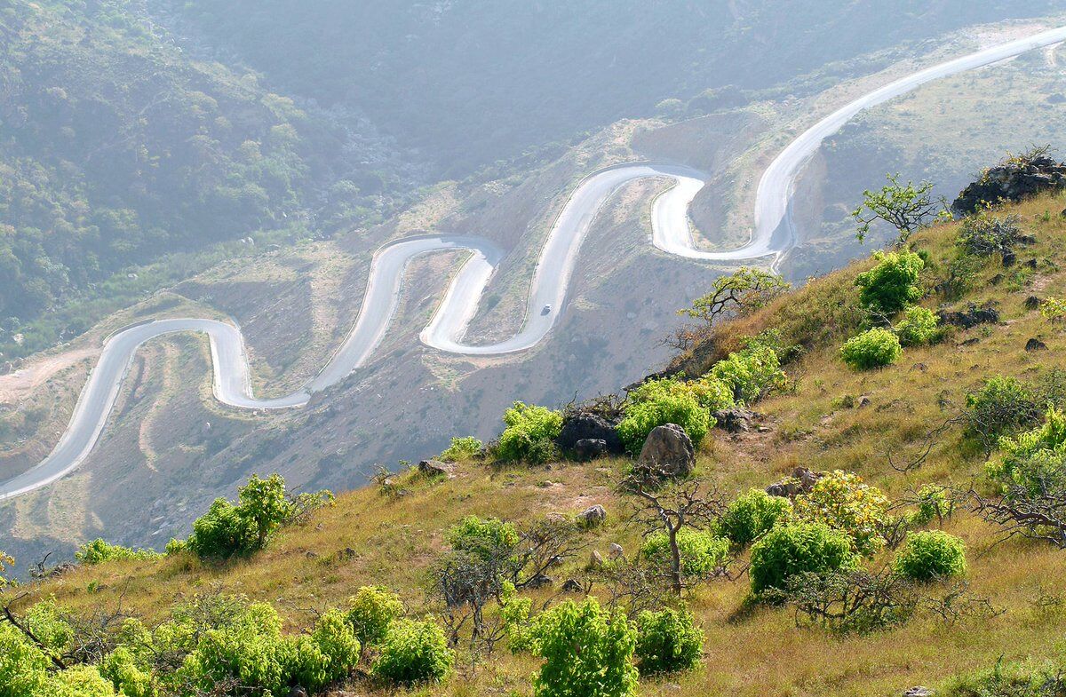 A winding mountain road with lush greenery and rocky terrain.