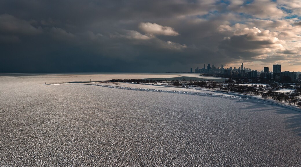 Aerial panorama of the Lake Michigan shoreline on the north side of Chicago covered in frozen ice 'pancakes' as clouds move past the downtown skyline in the distance and the sun begins to set.