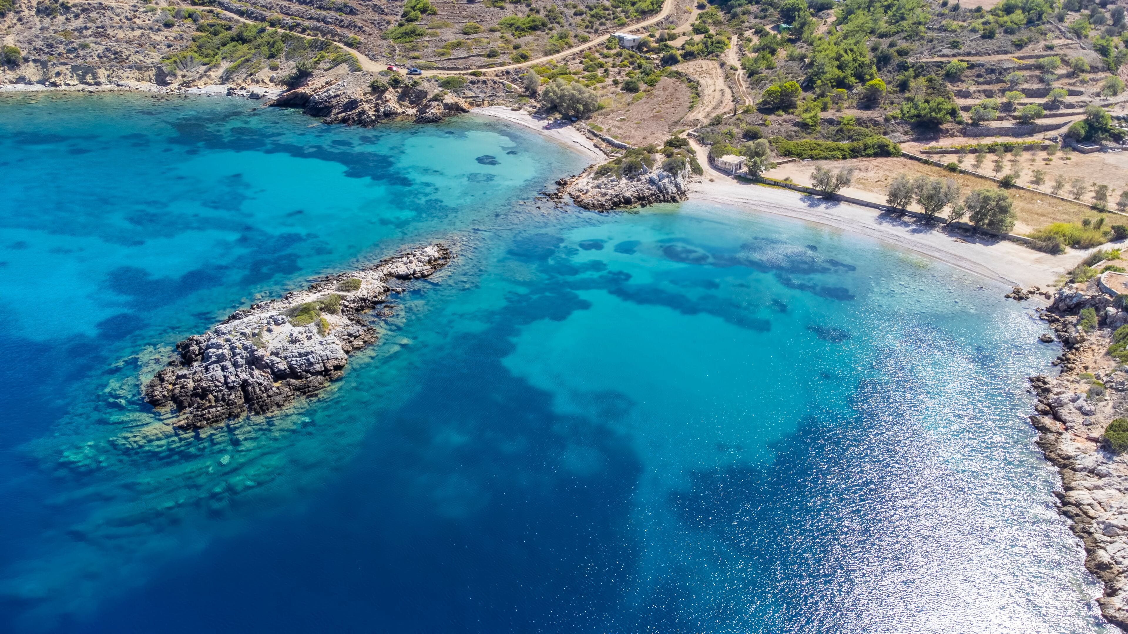 A coastal landscape with clear turquoise waters, rocky outcrops, and terraced fields.