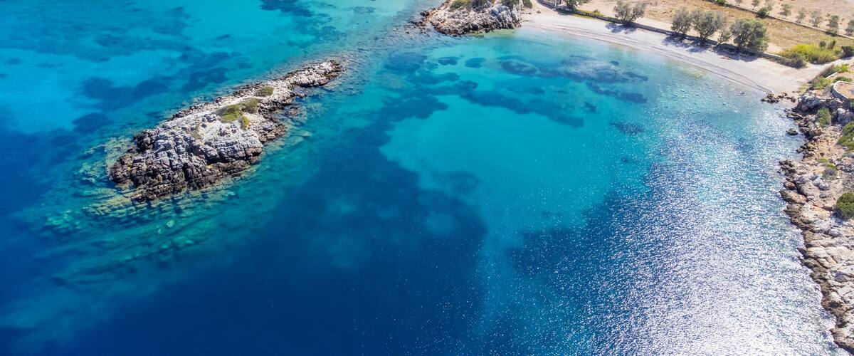 A coastal landscape with clear turquoise waters, rocky outcrops, and terraced fields.