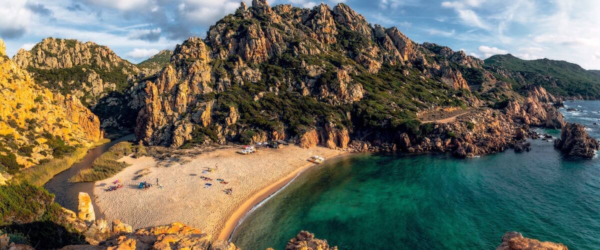 A coastal landscape with a rocky mountain, clear turquoise waters, and a sandy beach.