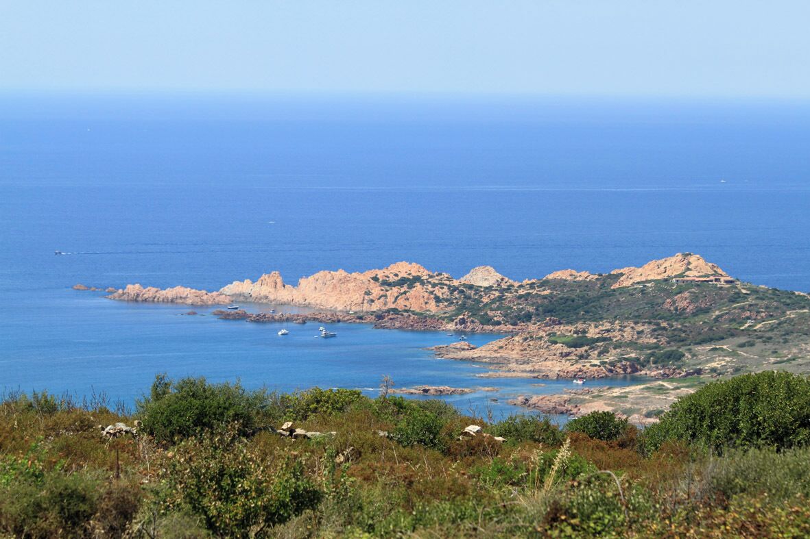 A coastal landscape with rocky hills and a clear blue sea.