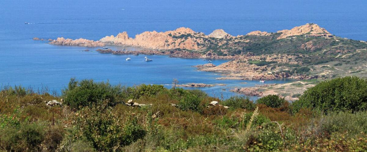 A coastal landscape with rocky hills and a clear blue sea.