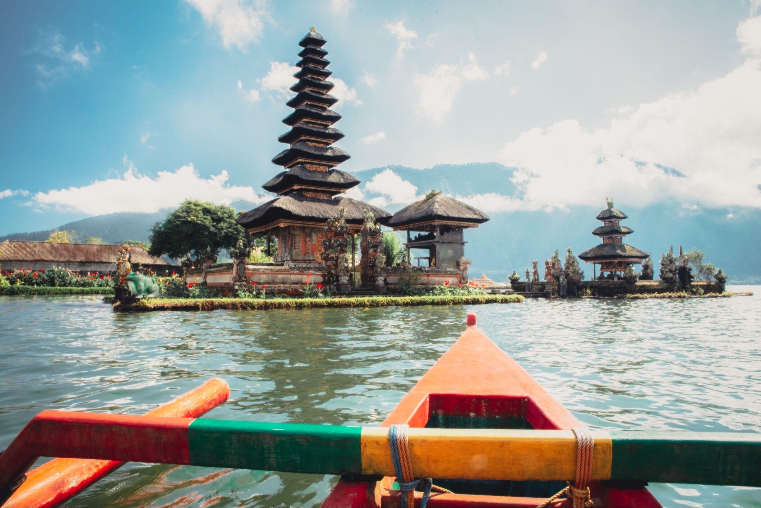A traditional Balinese temple with tiered roofs on a lake, viewed from a boat.