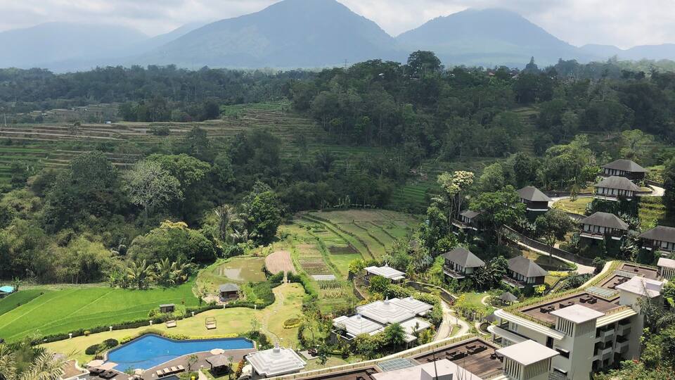 A resort with a swimming pool, terraced fields, and mountains in the background.