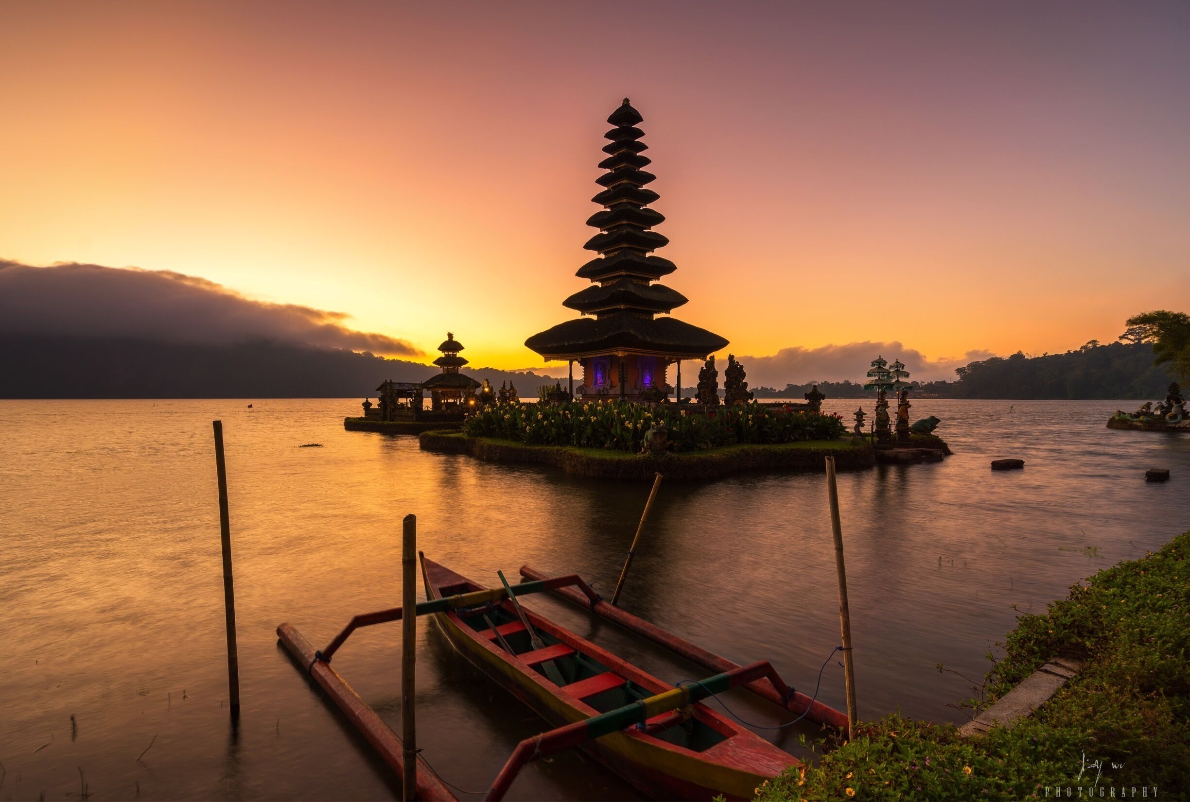A traditional temple with a tiered roof, a calm lake, and a sunset.