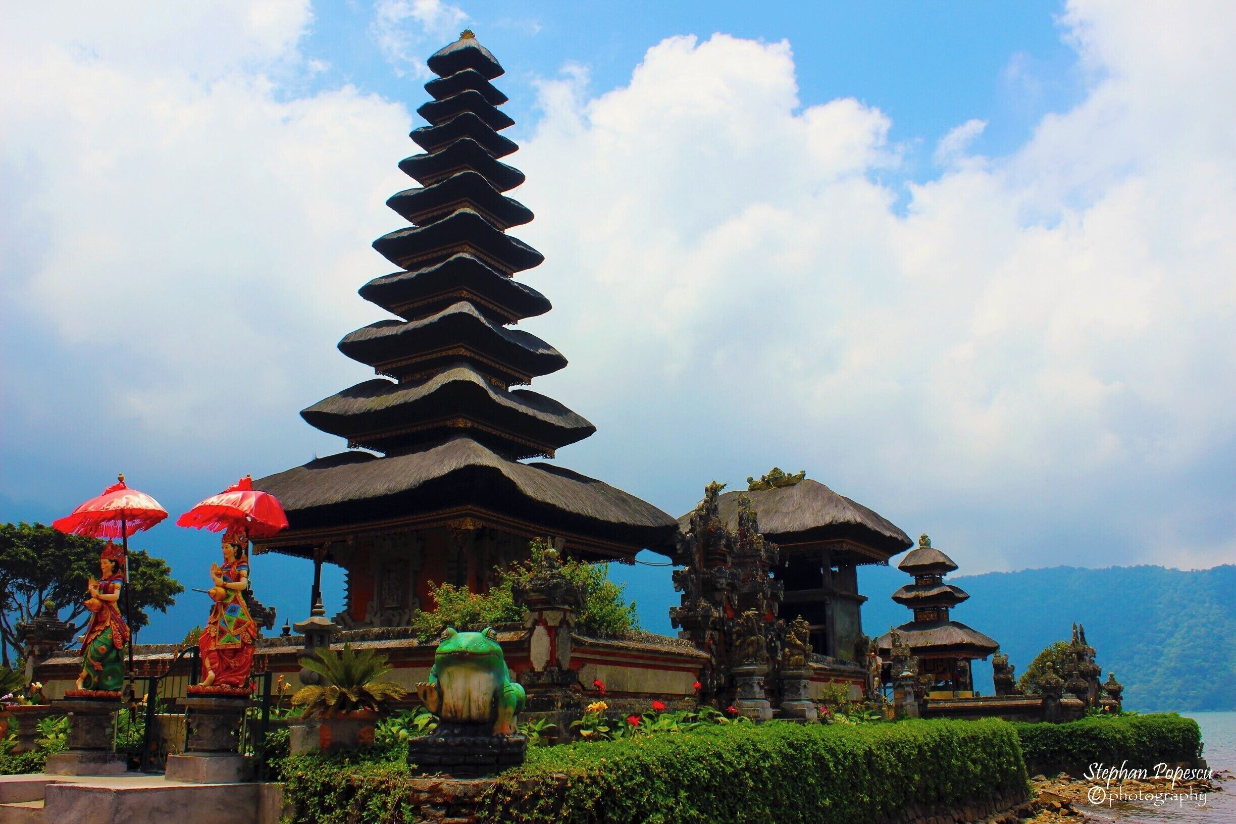 A traditional Balinese temple with tiered roofs, surrounded by lush greenery and a clear blue sky.
