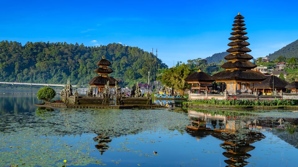 A serene lake with traditional pagodas and a bridge in the background.