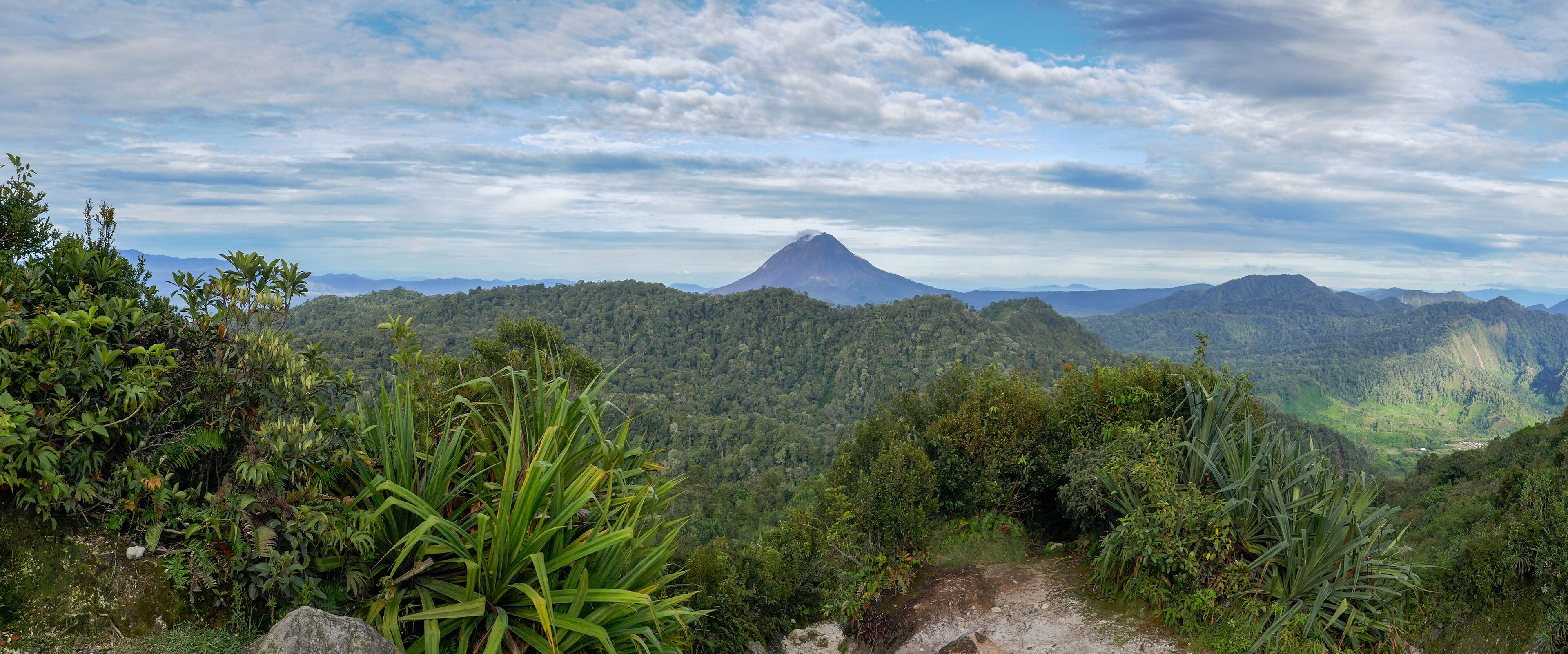 Scenic panoramic view on dense tropical forest with smoking Gunung Sinabung volcano in the distance, near Berastagi, North Sumatra, Indonesia