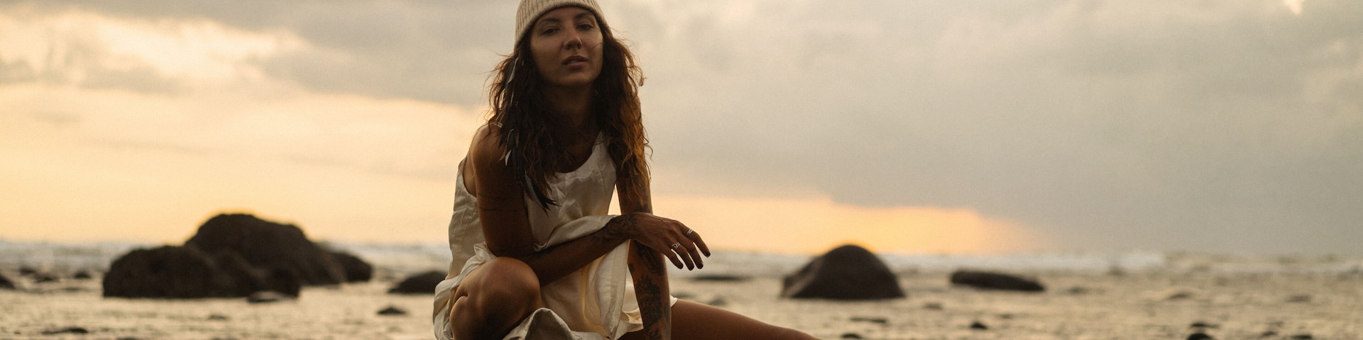 Una persona sentada en una playa rocosa con el océano al fondo.