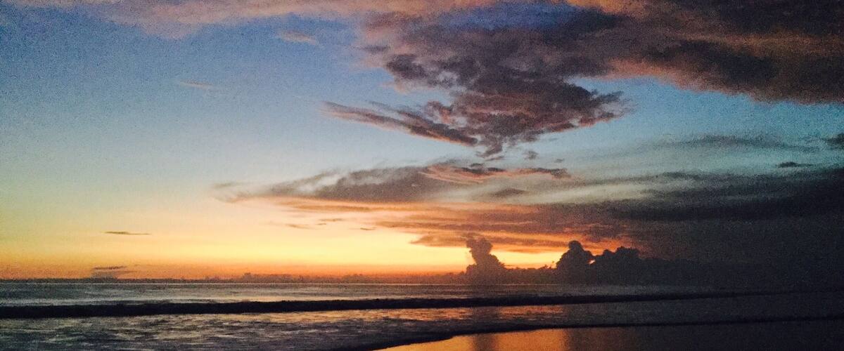 A beach at sunset with waves and a cloudy sky.