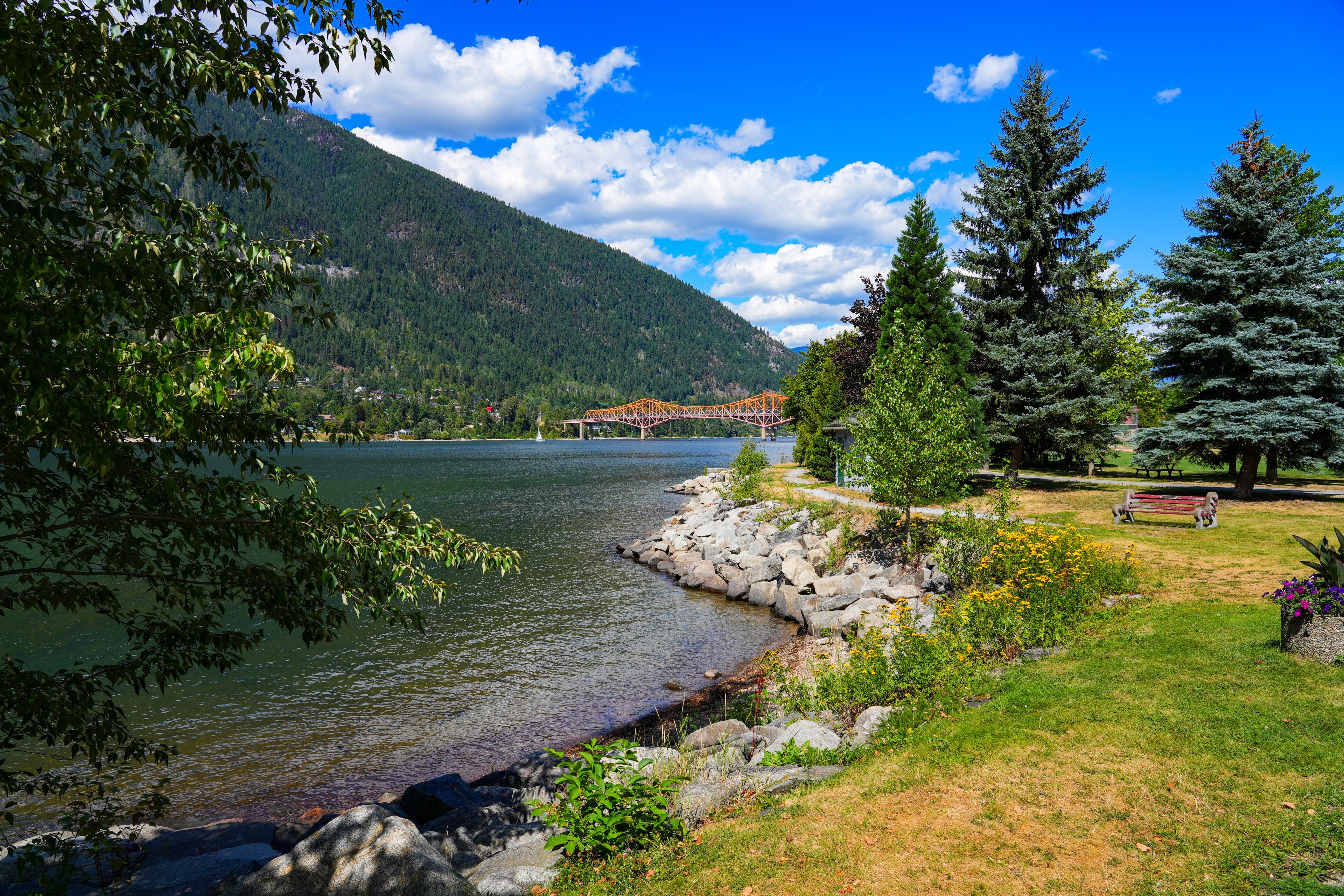 A lake surrounded by mountains, a bridge, and a park with benches.