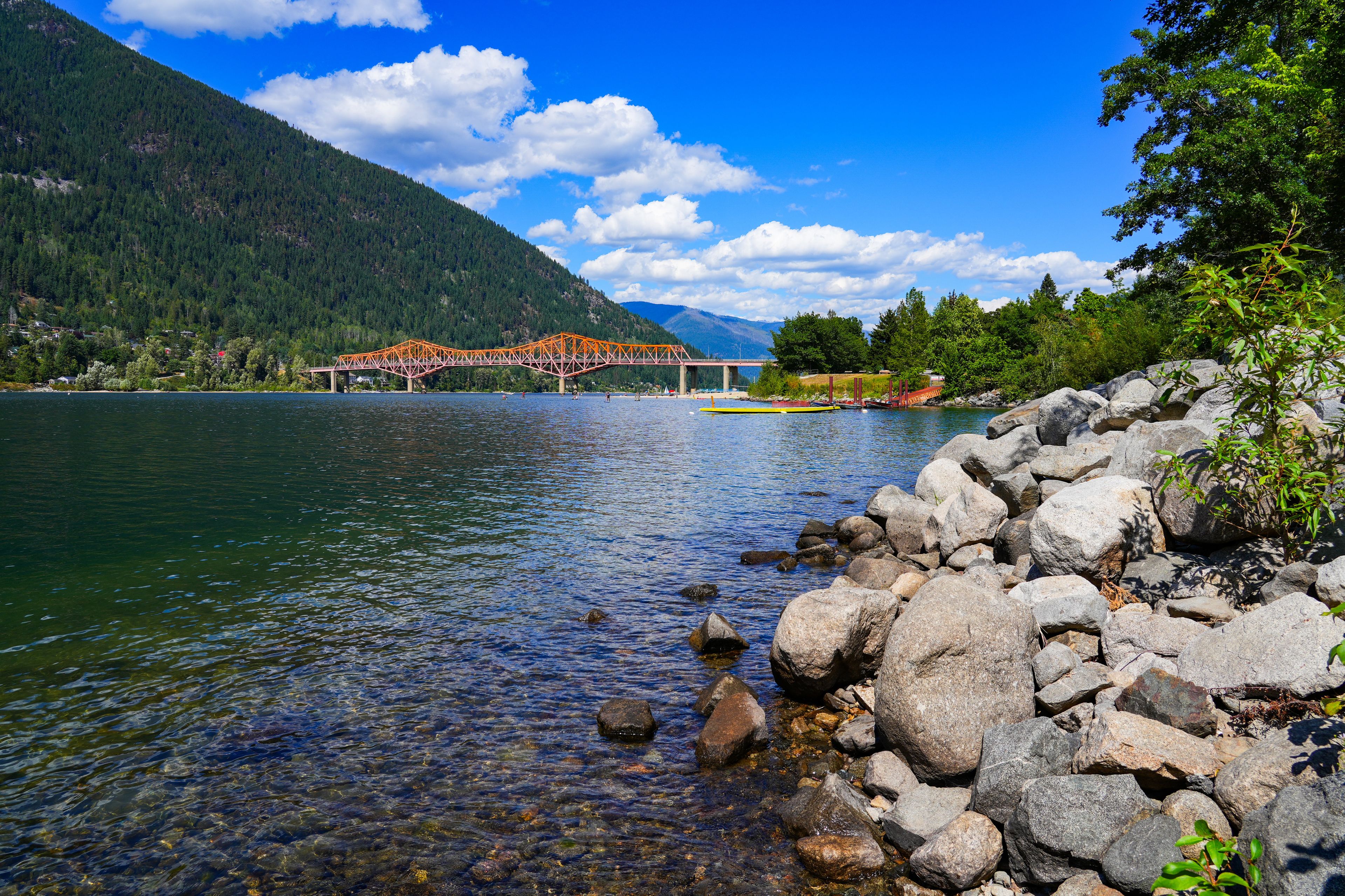 A bridge over a calm river, surrounded by mountains and rocky shores.