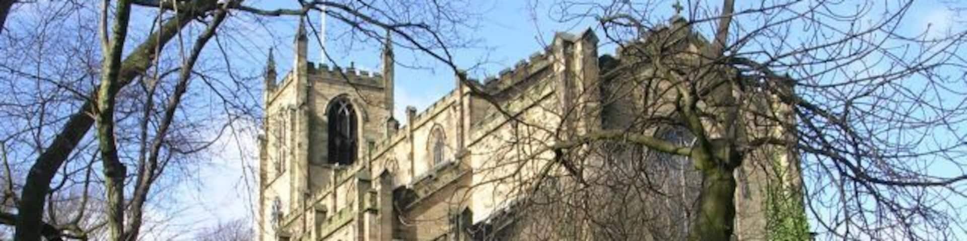 A historic church with a large tower and arched windows, surrounded by trees and a stone wall.