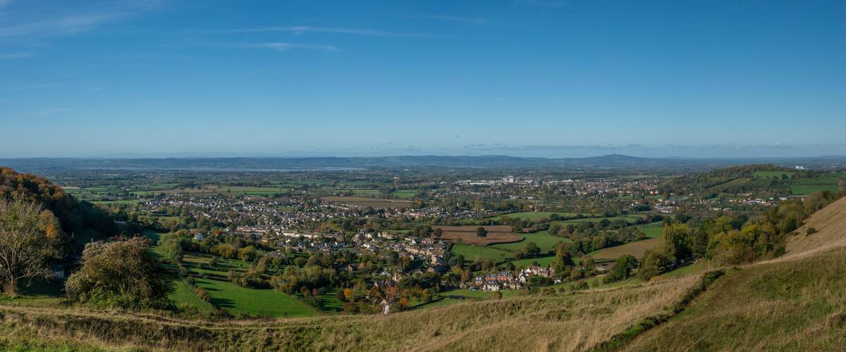 A panoramic view of a town nestled in a valley with rolling hills and a clear blue sky.