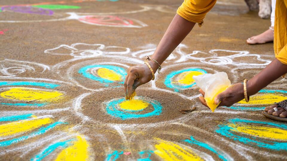A person drawing a colorful rangoli on the ground.
