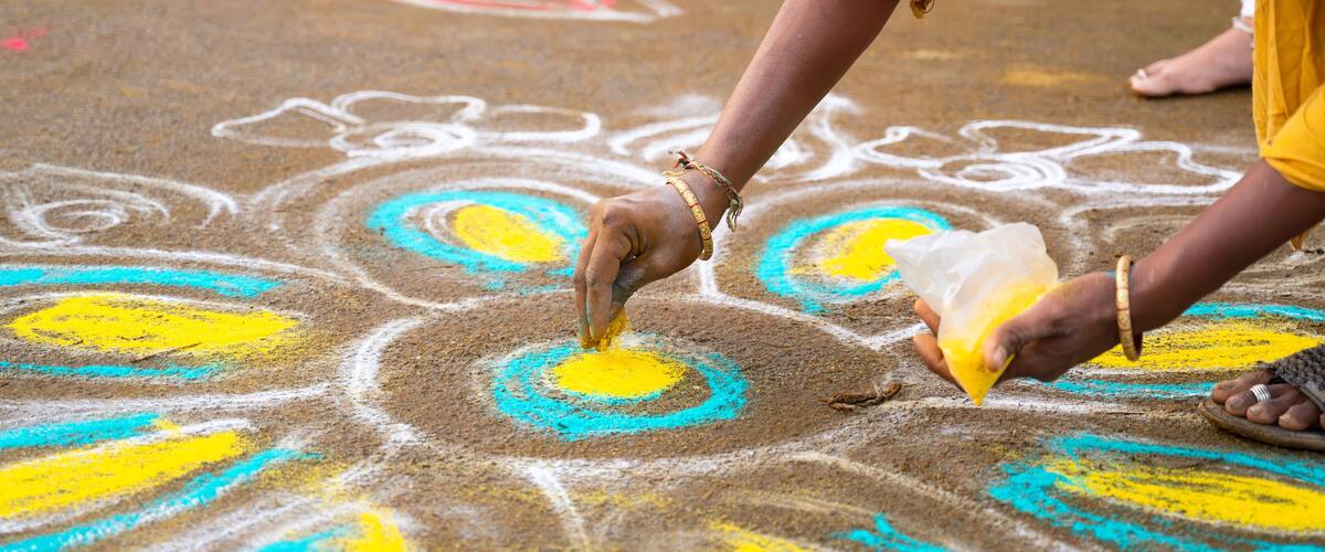 A person drawing a colorful rangoli on the ground.