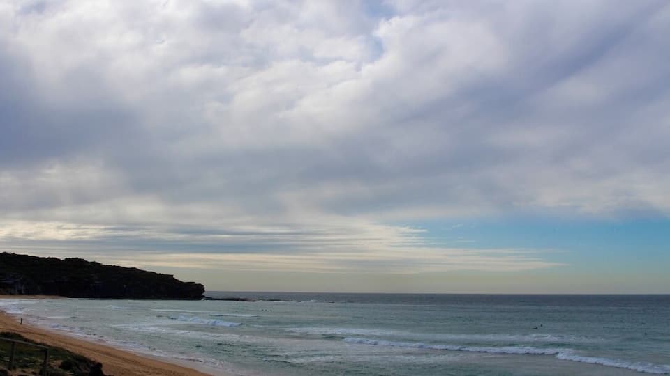 A beach with waves, a sandy shore, and a cloudy sky.