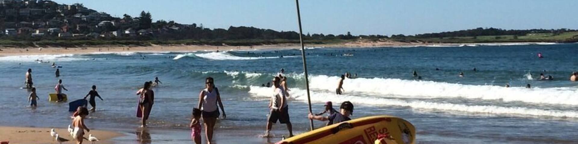A beach with a lifeguard stand, a lifeguard flag, a yellow surfboard, a beach towel, and a beach chair.