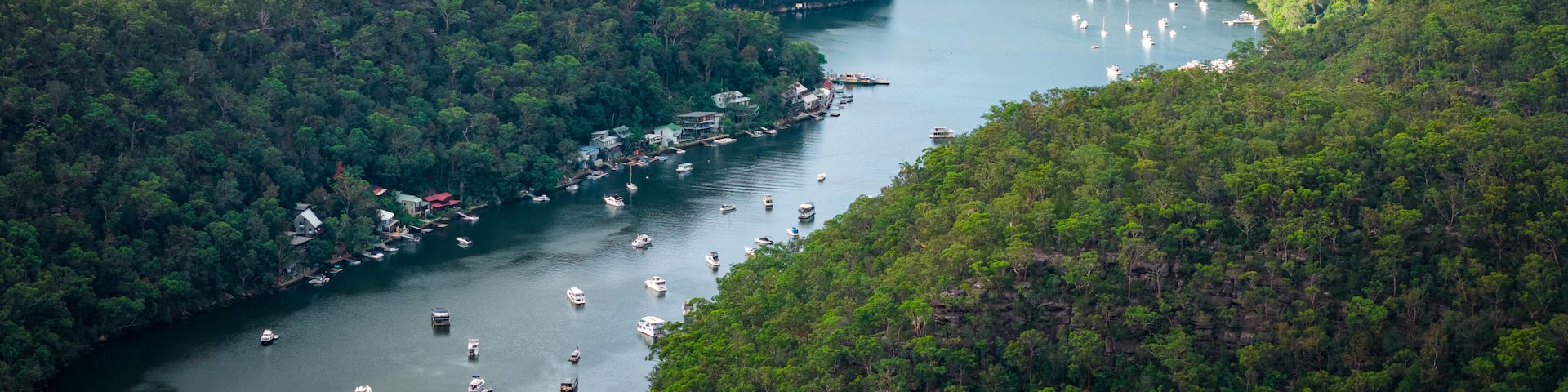 A river winding through a densely forested valley with numerous boats anchored along its banks.