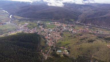 An aerial view of a town nestled in a valley with surrounding hills, a river, and a bridge.