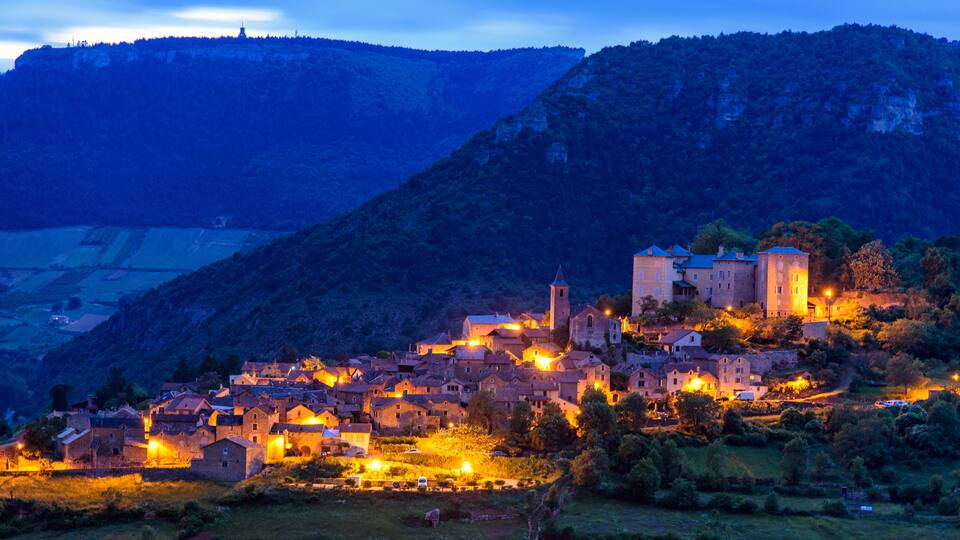 A village at dusk with illuminated buildings and a prominent church on a hillside.