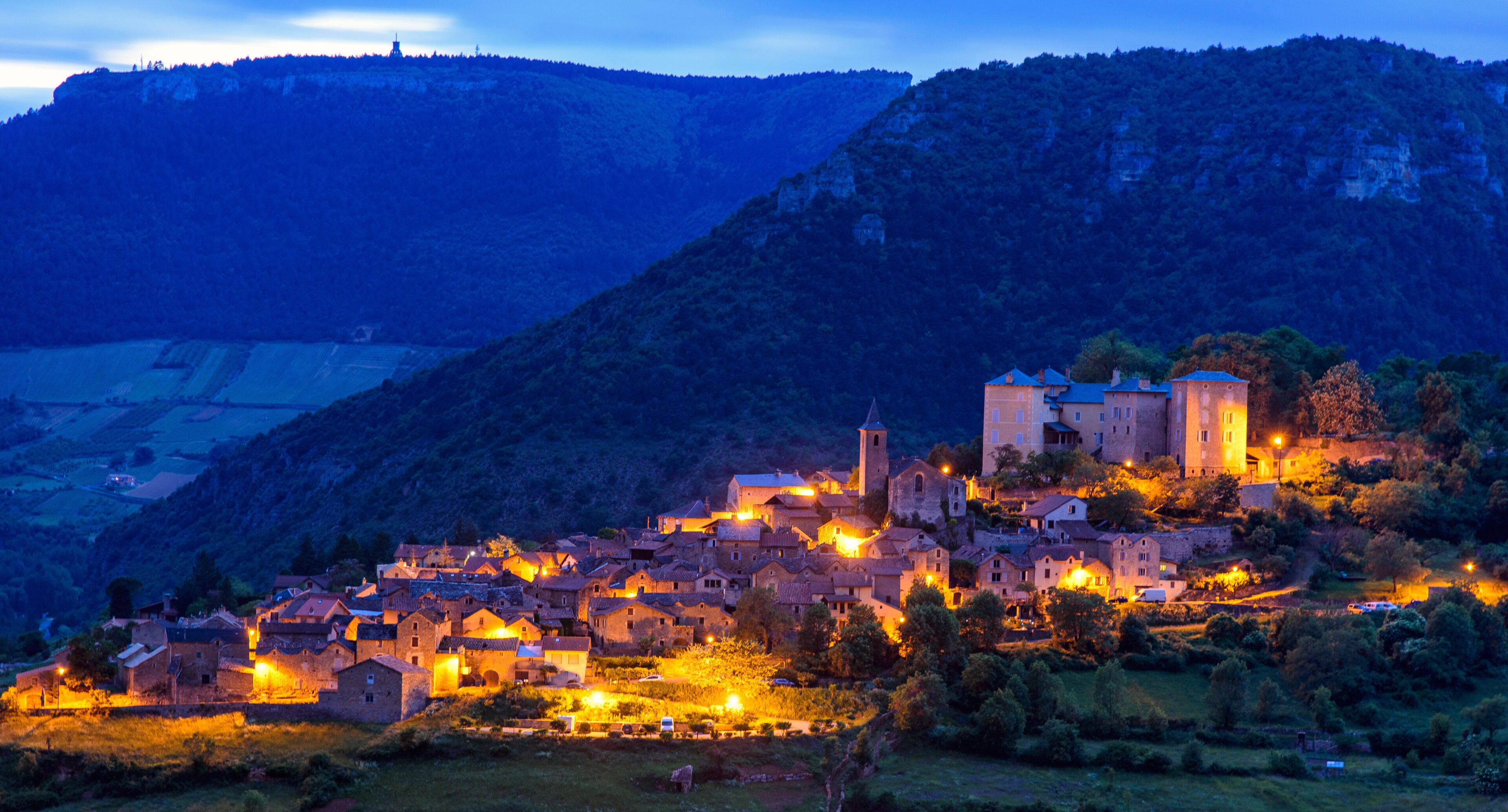 A village at dusk with illuminated buildings and a prominent church on a hillside.
