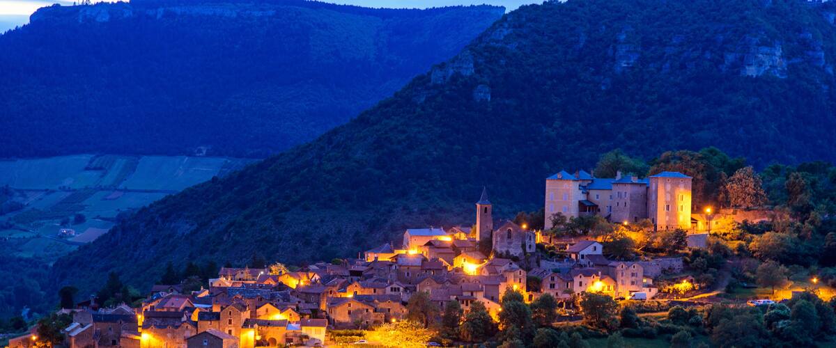 A village at dusk with illuminated buildings and a prominent church on a hillside.