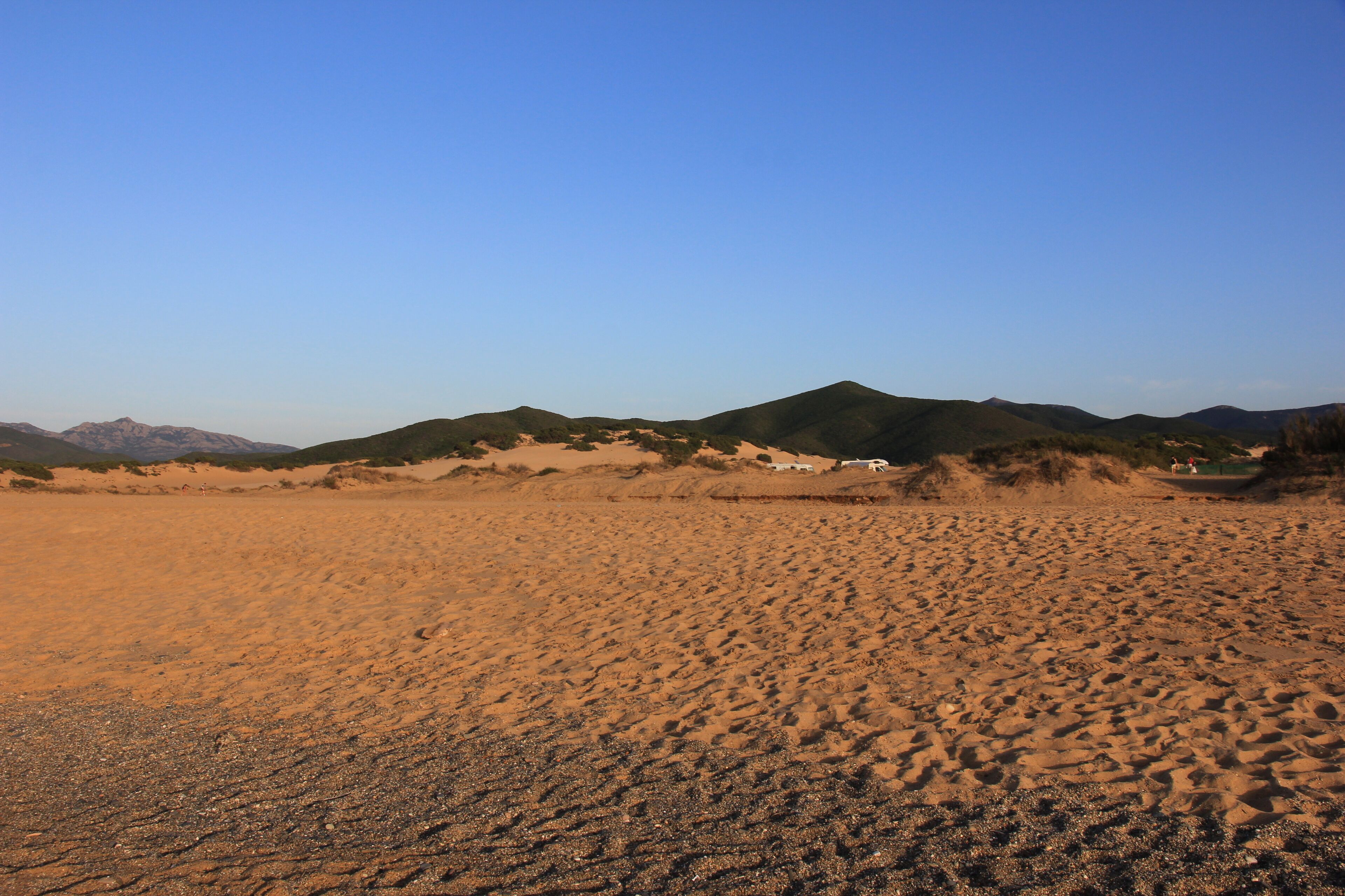 A desert landscape with sand dunes and distant mountains under a clear sky.