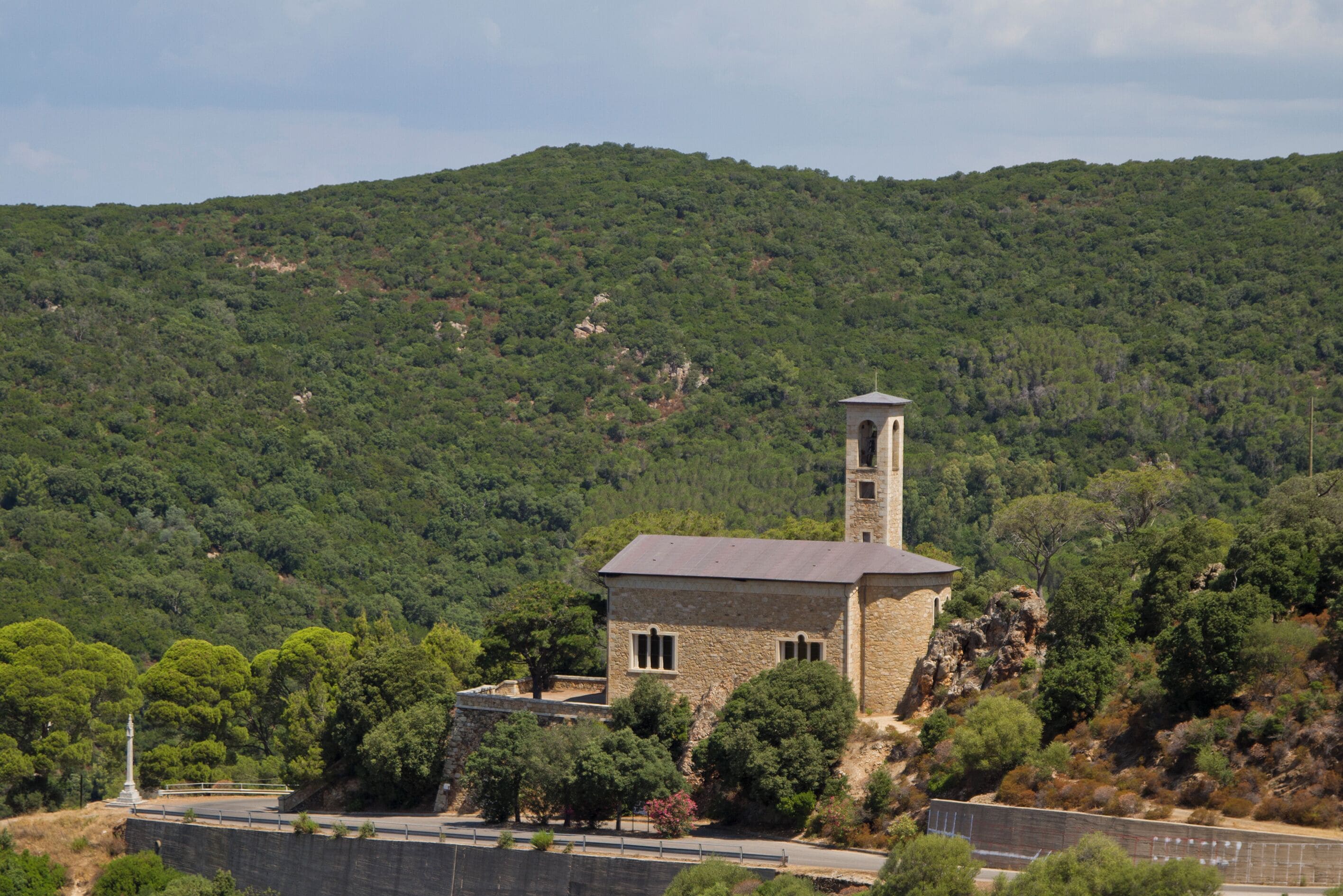 A stone tower with a bell on a hill surrounded by dense green forest.