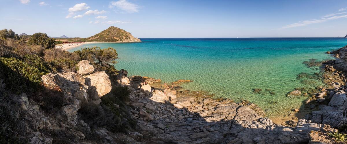 A coastal landscape with rocky cliffs, clear turquoise waters, and a distant island.