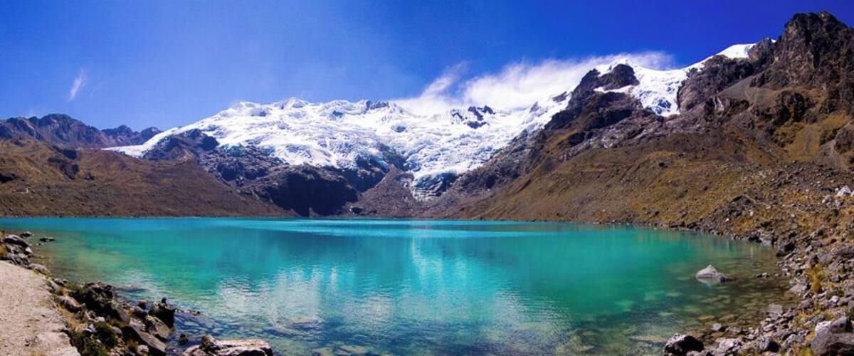 A turquoise lake surrounded by snow-capped mountains and rocky terrain.