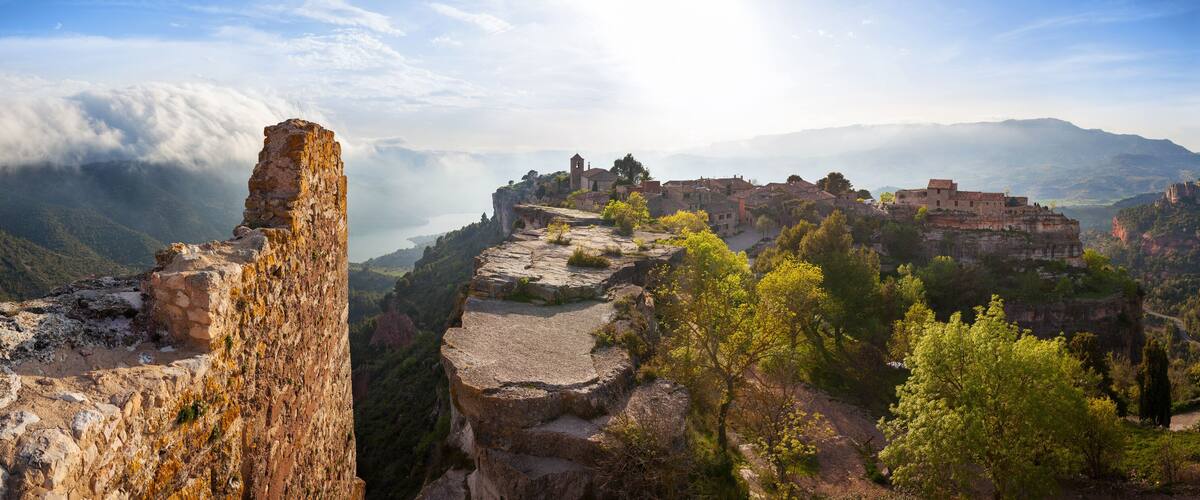 A historic village perched on a cliffside with ancient ruins and lush greenery.