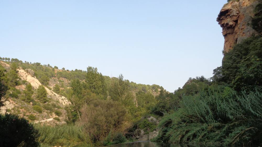 A river flowing through a valley with rocky cliffs and dense greenery.