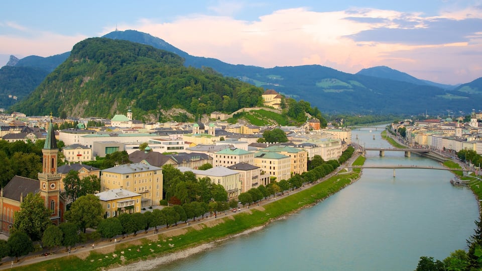 A riverside cityscape with historic buildings, a prominent church, and a hill with a tower in the background.