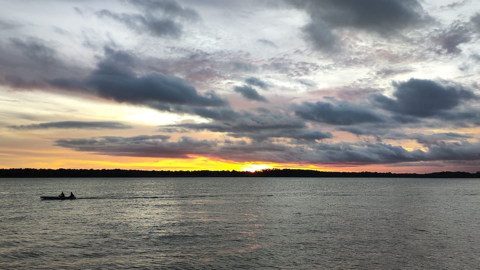 A sunset over a body of water with a silhouette of a boat and a distant shoreline.