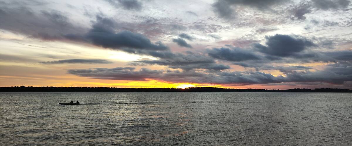 A sunset over a body of water with a silhouette of a boat and a distant shoreline.