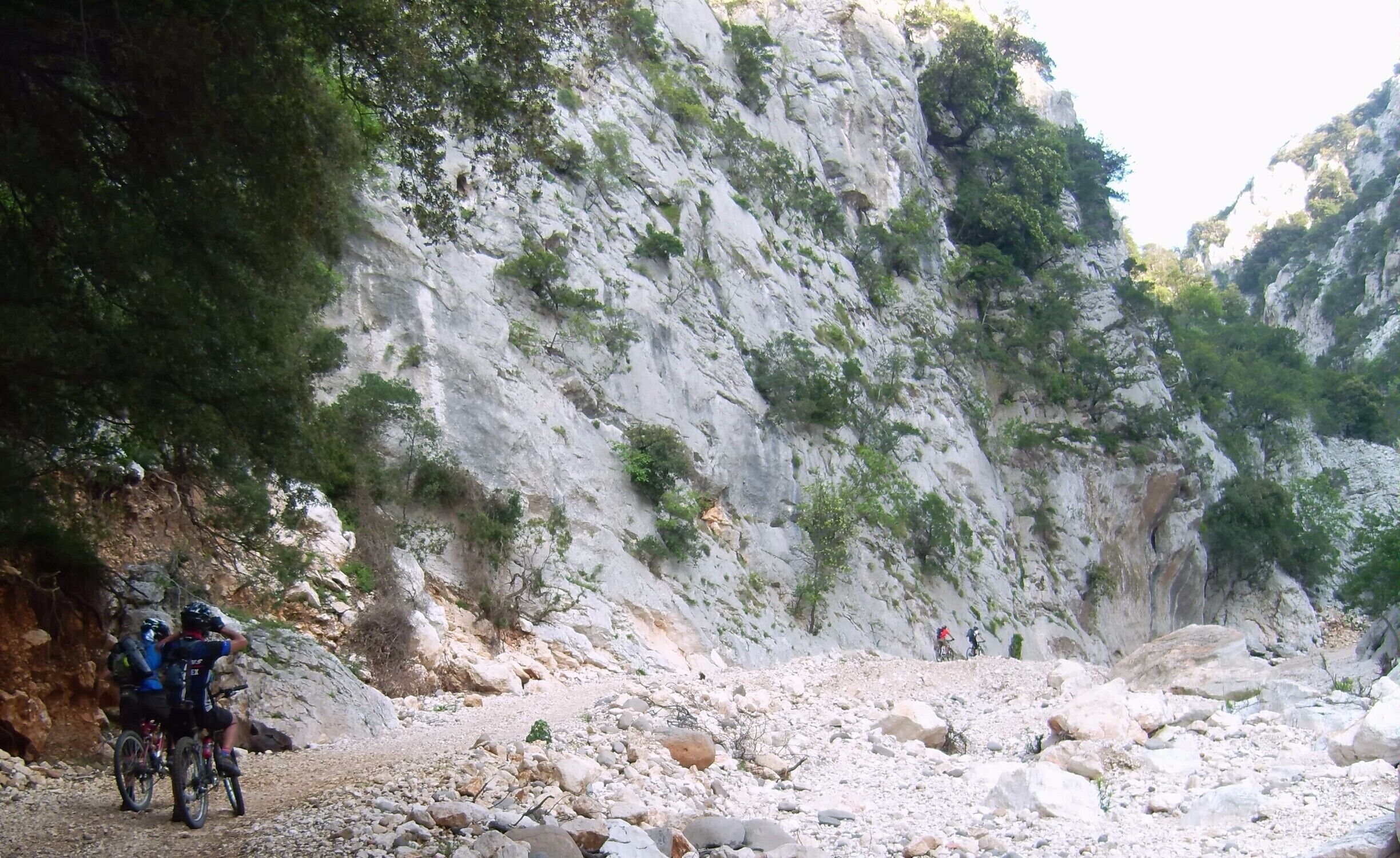 A rocky mountain trail with cyclists and a steep cliff.