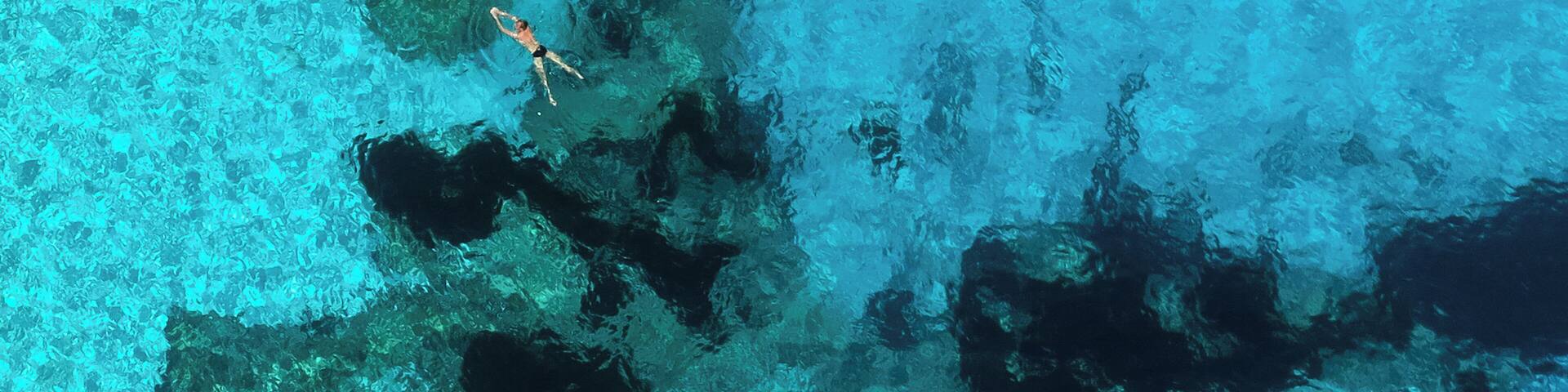 Swimmer off Cala Goloritze, a secluded Sardinian beach, as seen from the top of Aguglia di Goloritzé, a 500 foot, limestone spire above the beach. While the view isn't possible without a technical rock climb up pristine limestone, the beach can be reached with a three mile hike down through the woods. #AboveItAll