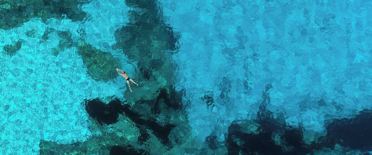 A clear blue sea with a person swimming.