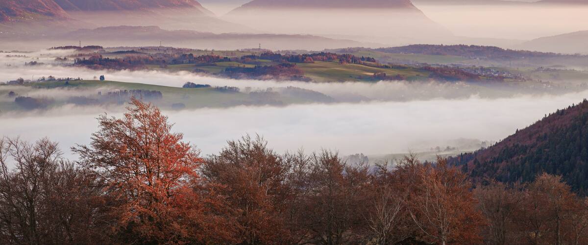 A mountainous landscape with a valley, mist, and autumn-colored trees.