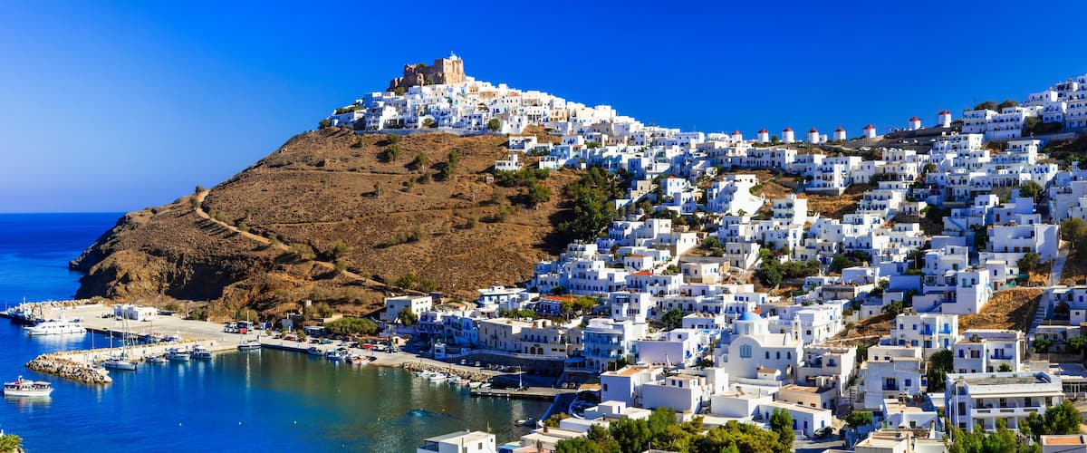 A coastal town with white buildings, a harbor, and a hill with a castle.
