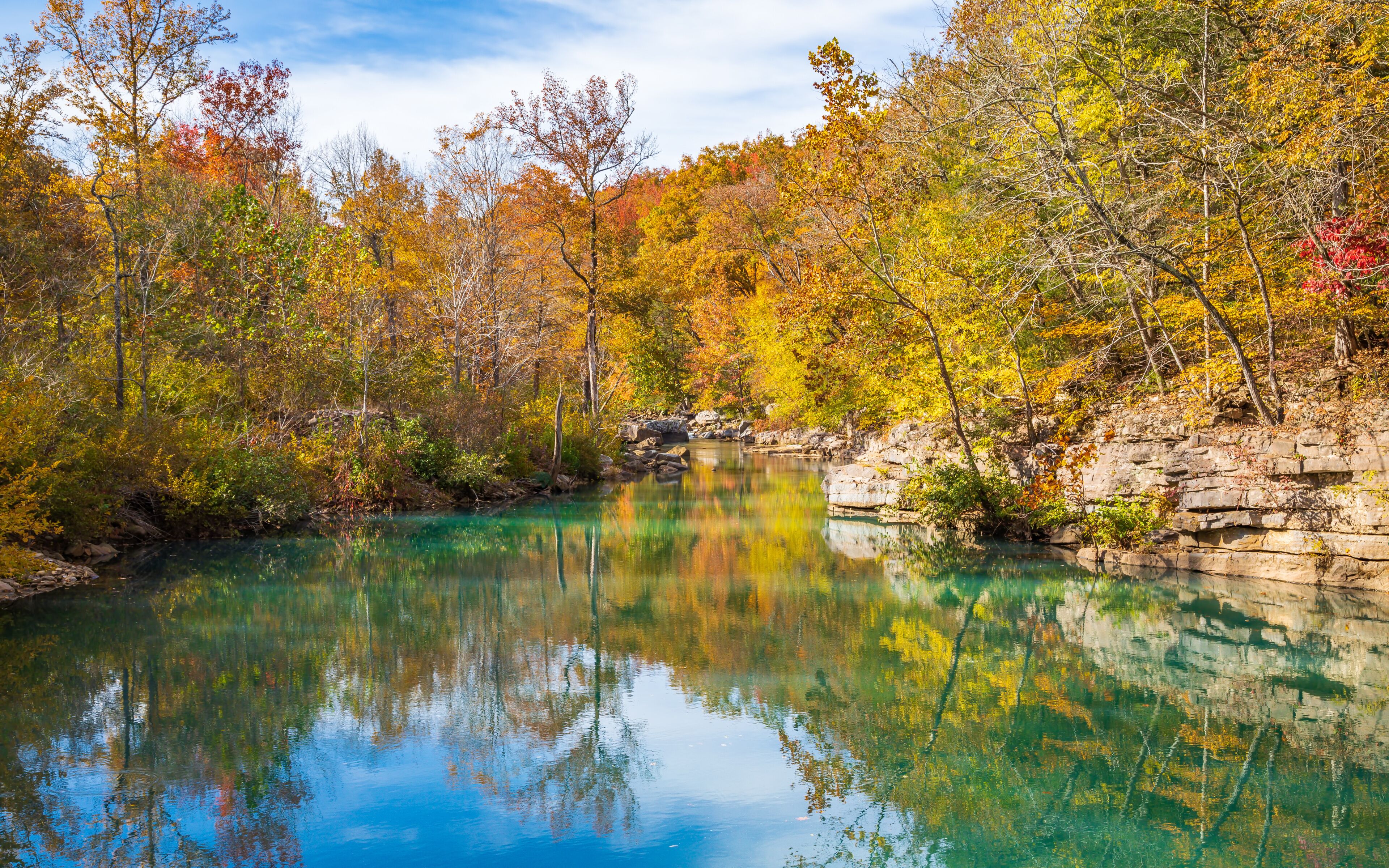 A clear lake surrounded by autumn-colored trees and rocky cliffs.