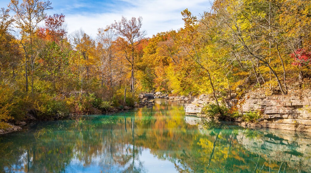 A clear lake surrounded by autumn-colored trees and rocky cliffs.