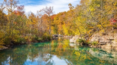 Um lago límpido rodeado por árvores com cores de outono e penhascos rochosos.