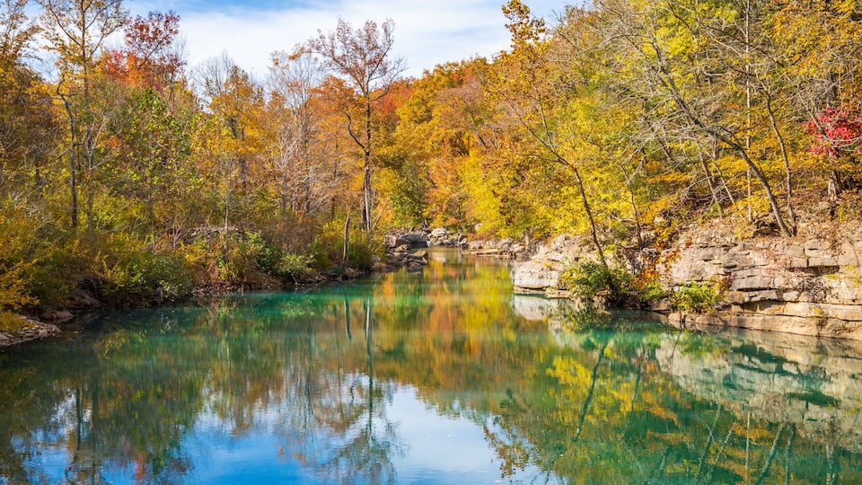 A clear lake surrounded by autumn-colored trees and rocky cliffs.