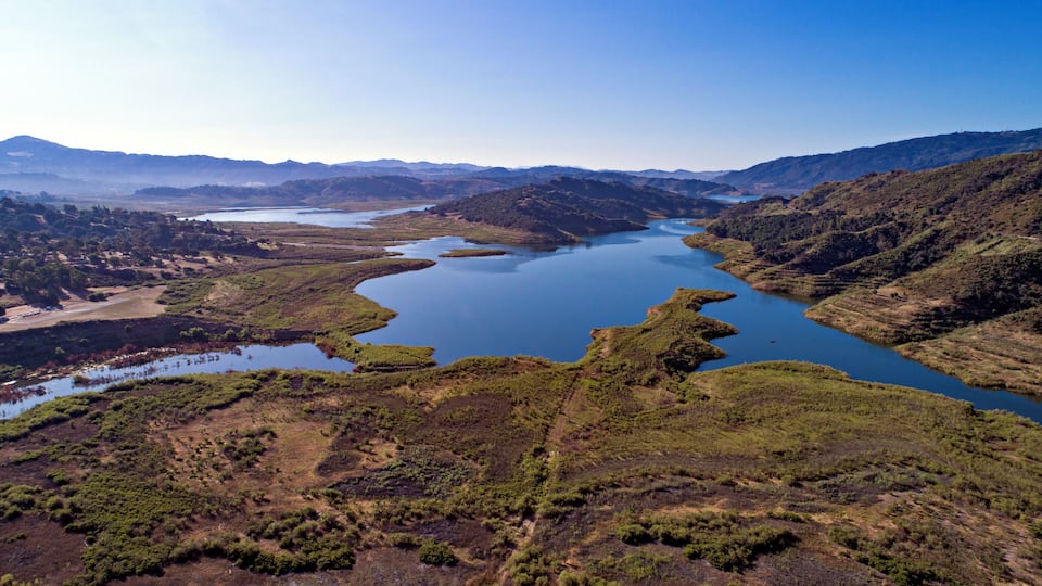 A river winding through a hilly landscape with patches of greenery and a clear blue sky.
